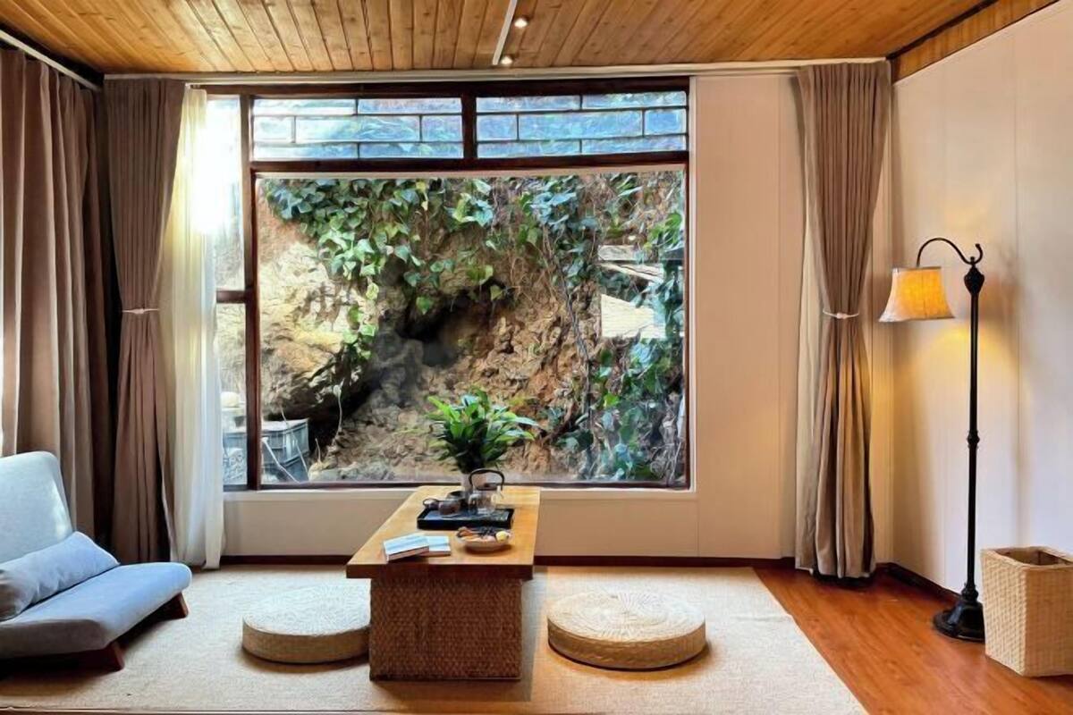A room with a large window, a sofa, a small table with a plant, and a lamp.
