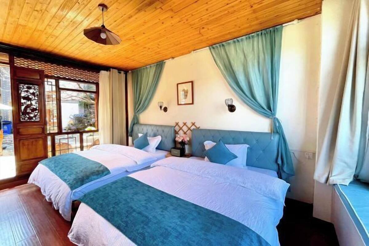 A room with two beds, wooden ceiling, and a window with curtains.
