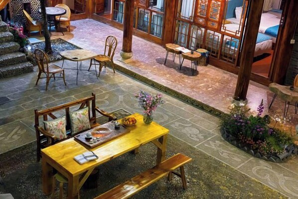A spacious indoor area with a wooden table, chairs, and a bench. There are multiple seating arrangements and a small garden area with plants.