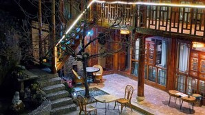 Un bâtiment traditionnel en bois, doté d’une cour, d’escaliers en pierre et d’un espace extérieur aménagé pour s’asseoir.