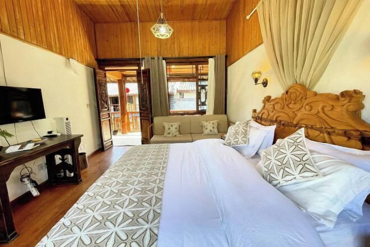 A bedroom with a wooden ceiling, a bed with patterned bedding, a television, and a desk with shoes.