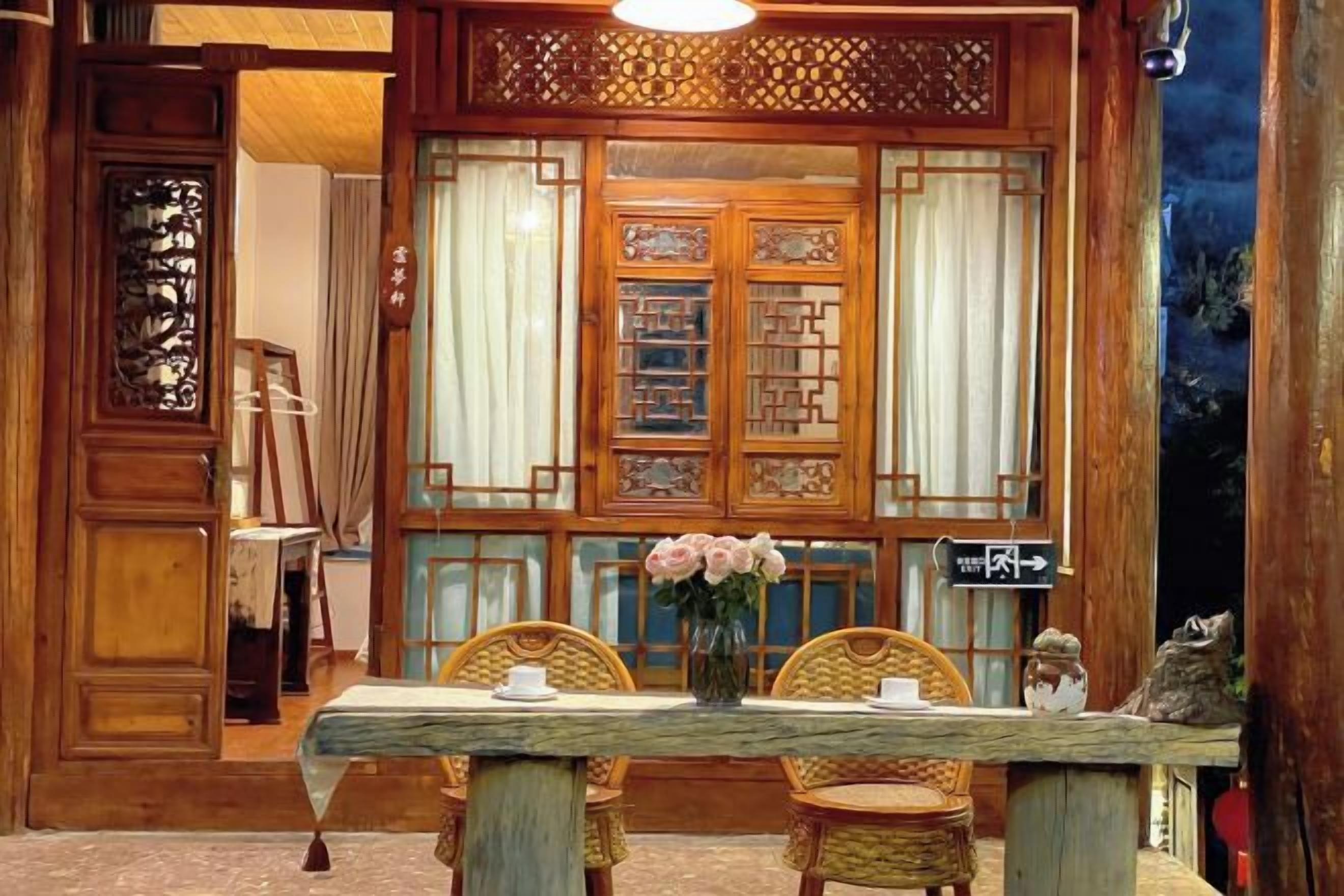 A traditional wooden room with a table set for two, a vase with flowers, and a decorative screen with intricate patterns.