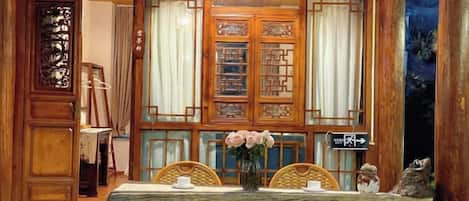 A traditional wooden room with a table set for two, a vase with flowers, and a decorative screen with intricate patterns.