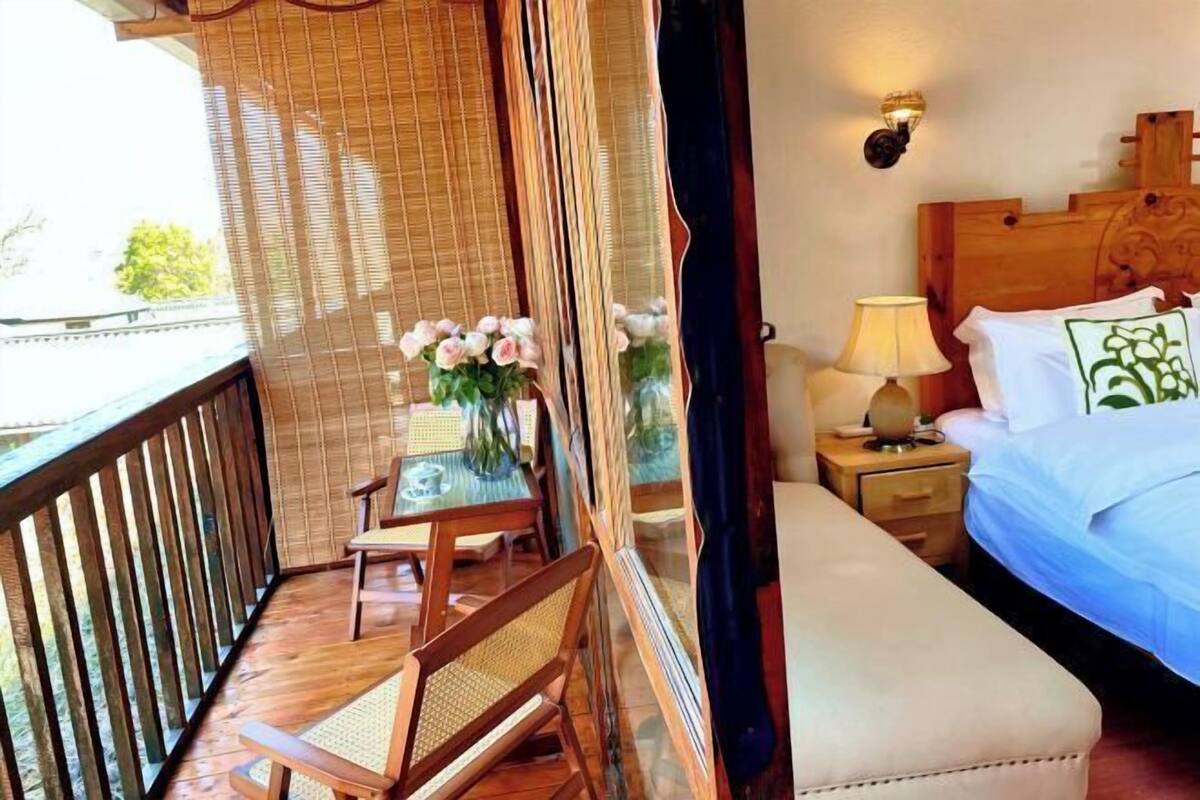 A balcony with a table and chairs, a bed with a nightstand, and a wall-mounted lamp.