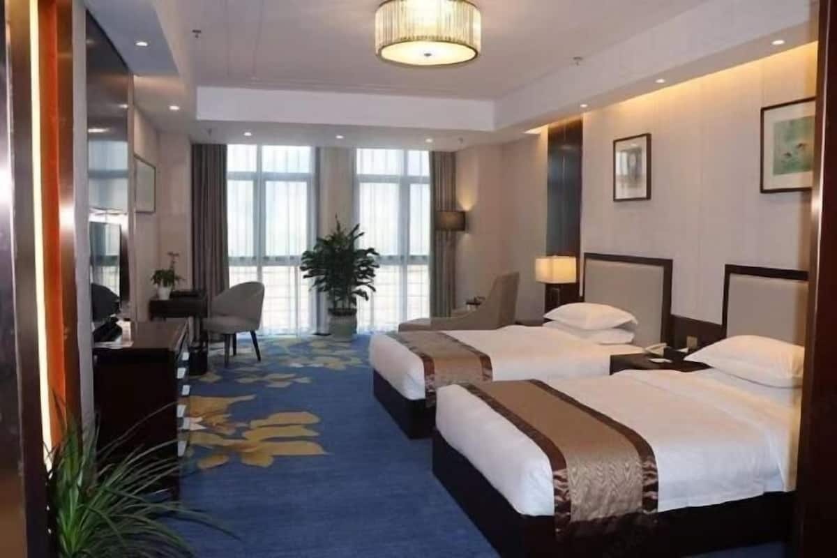 A hotel room with two beds, a desk, a chair, and a large window.