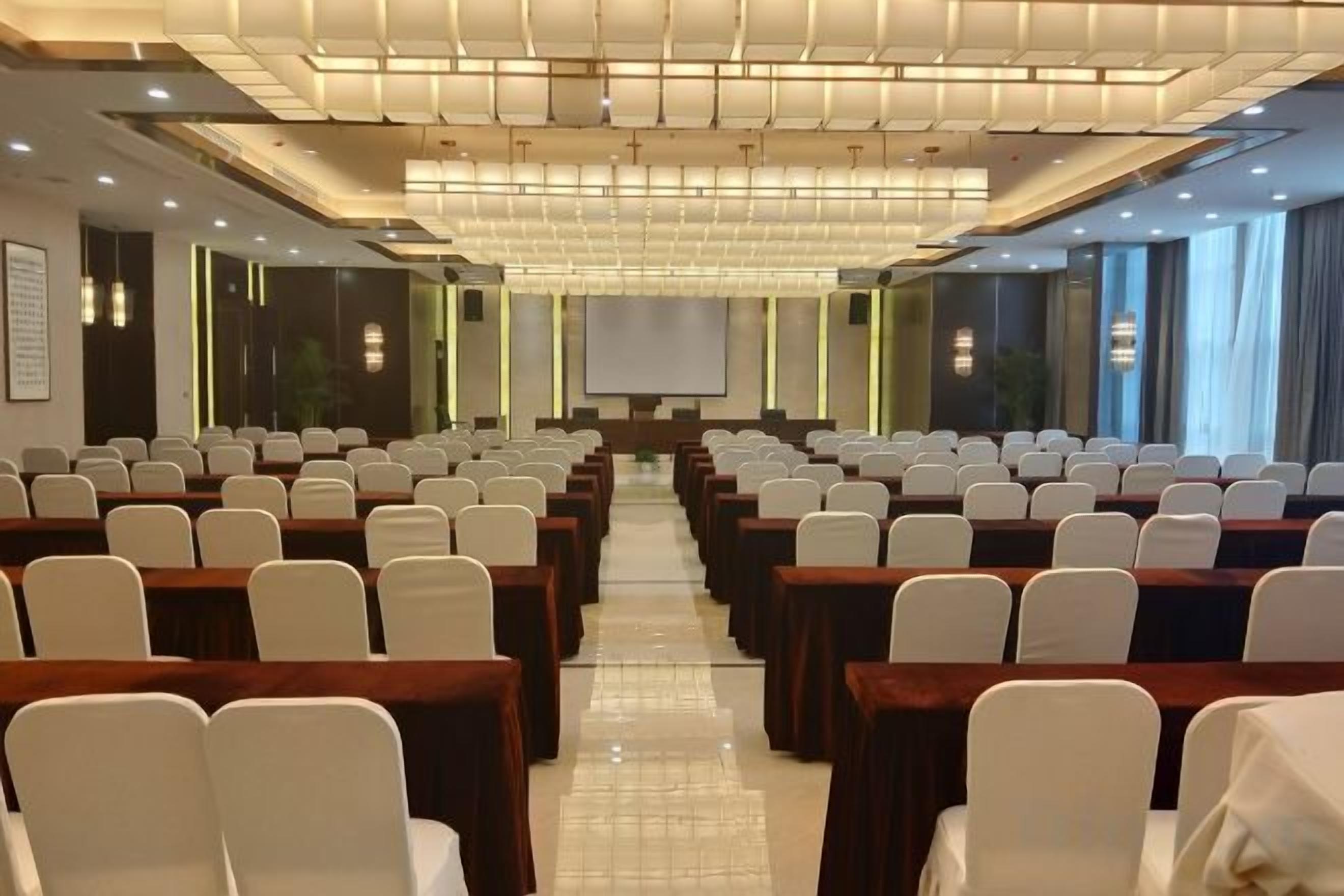A conference room with rows of chairs and tables, a projector screen, and a large window.