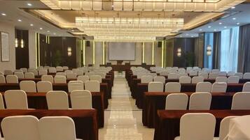 Un salón de conferencias con filas de sillas y mesas, una pantalla de proyector y un ventanal grande.