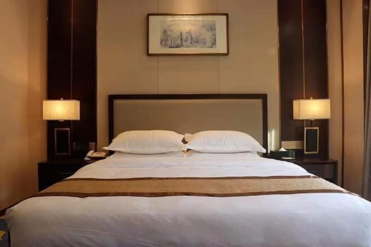 A hotel room with a large bed, two bedside lamps, a framed picture on the wall, and a wooden headboard.
