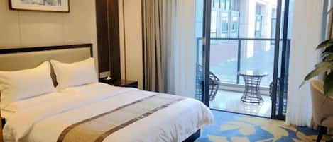 Habitación de hotel con una cama grande, vistas al exterior y un balcón con mesa y sillas.