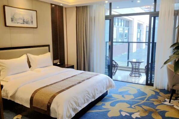 Habitación de hotel con una cama grande, vistas al exterior y un balcón con mesa y sillas.