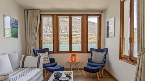 Et hyggeligt rum med et stort vindue, en sofa, to lænestole, et lille bord med tesæt og en lampe.