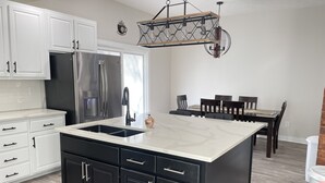 Eine moderne Küche mit Kochinsel, weißen Schränken, Edelstahlgeräten und einem Essbereich mit Holztisch und Stühlen.
