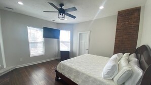 Ein Schlafzimmer mit einem Bett, einem Deckenventilator, einem Fenster und einer Wand mit Backsteinverkleidung.