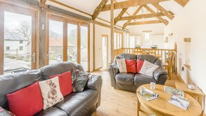 A spacious living area with a high ceiling and exposed wooden beams, furnished with leather sofas and a wooden coffee table. - 3 bedroom accommodation in Rackenford, near Tiverton (Rackenford, near Tiverton)