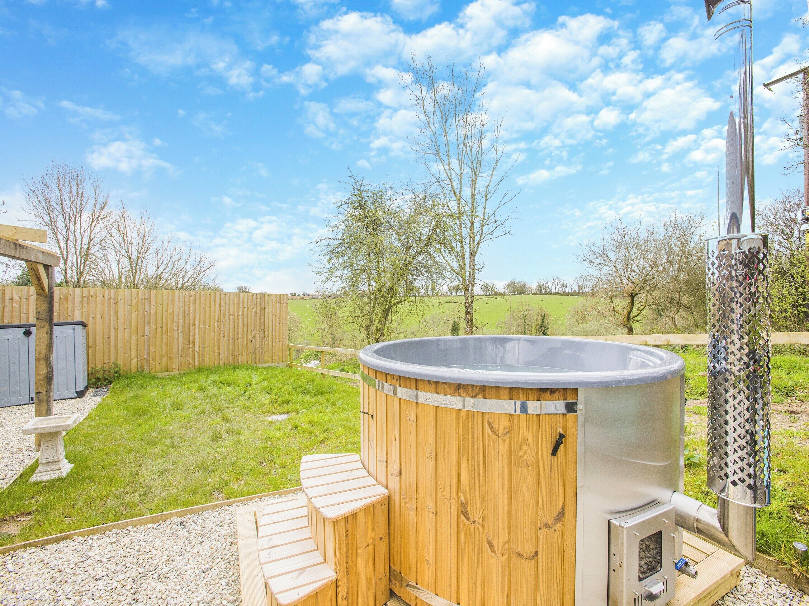 Un bain à remous avec des marches en bois et un réchauffeur en métal, entouré d’une terrasse en bois et d’une pelouse.
