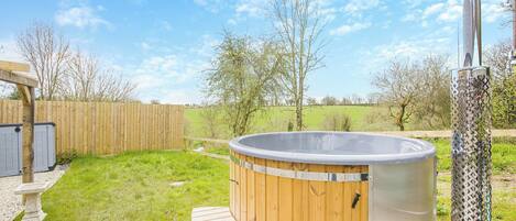 Un bain à remous avec des marches en bois et un réchauffeur en métal, entouré d’une terrasse en bois et d’une pelouse.