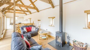 A cozy living room with a fireplace, wooden beams, a sofa, and a dining area. - 3 bedroom accommodation in Rackenford, near Tiverton (Rackenford, near Tiverton)