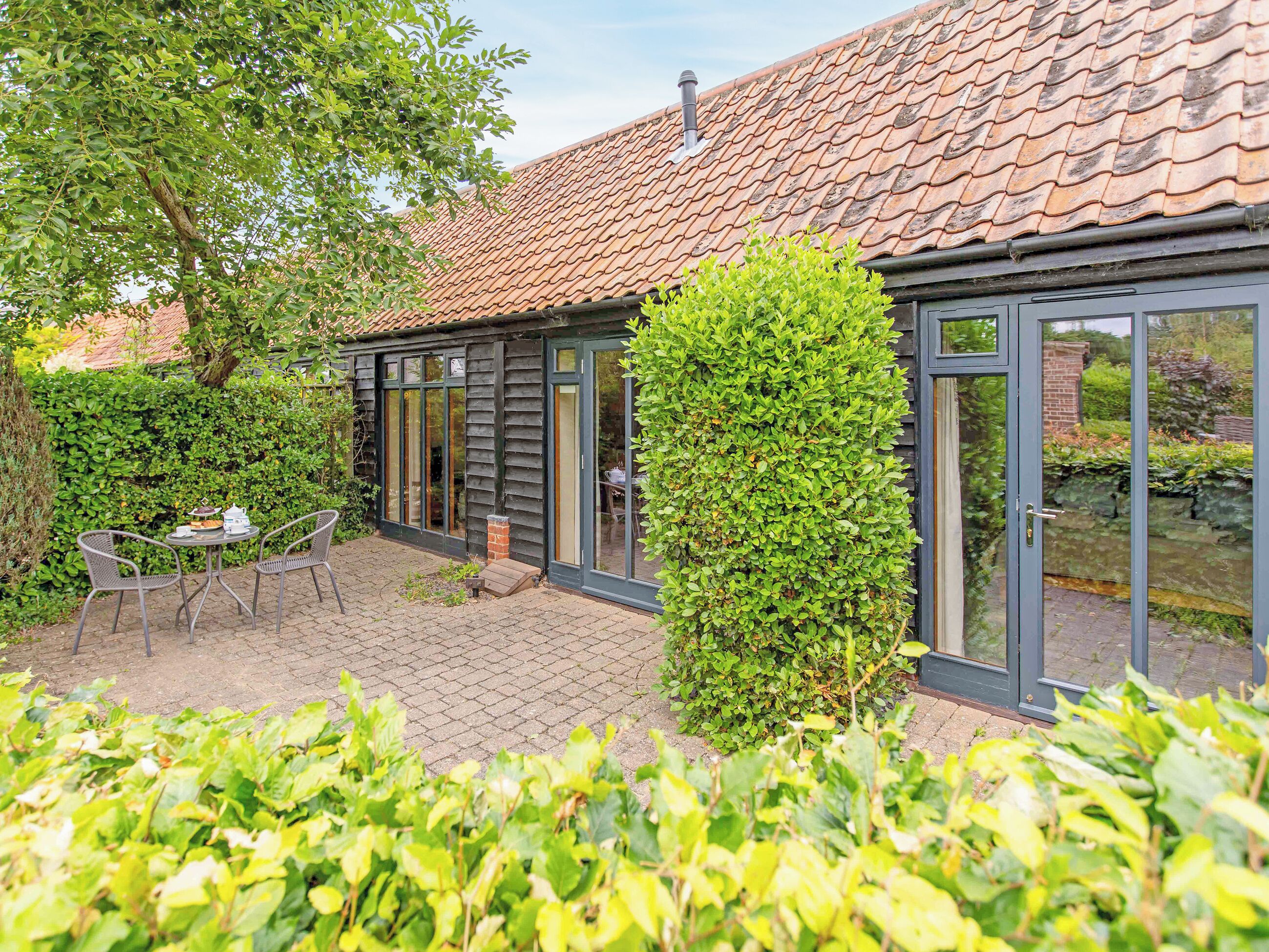A building with a tiled roof, a glass door, and a brick patio with outdoor furniture.