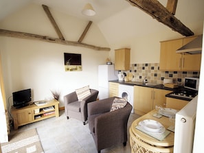 A compact living space with a kitchen, two sofas, a television, and a dining area with a table set for two.