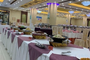 A banquet hall with tables set for a buffet, featuring various food stations and a large central serving area.