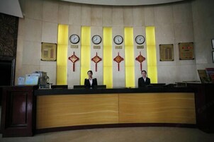 Un mostrador de recepción con dos recepcionistas, un reloj y decoraciones chinas tradicionales.