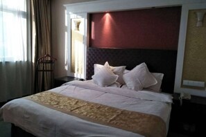 A hotel room with a large bed, a headboard, a nightstand, and a window with curtains.