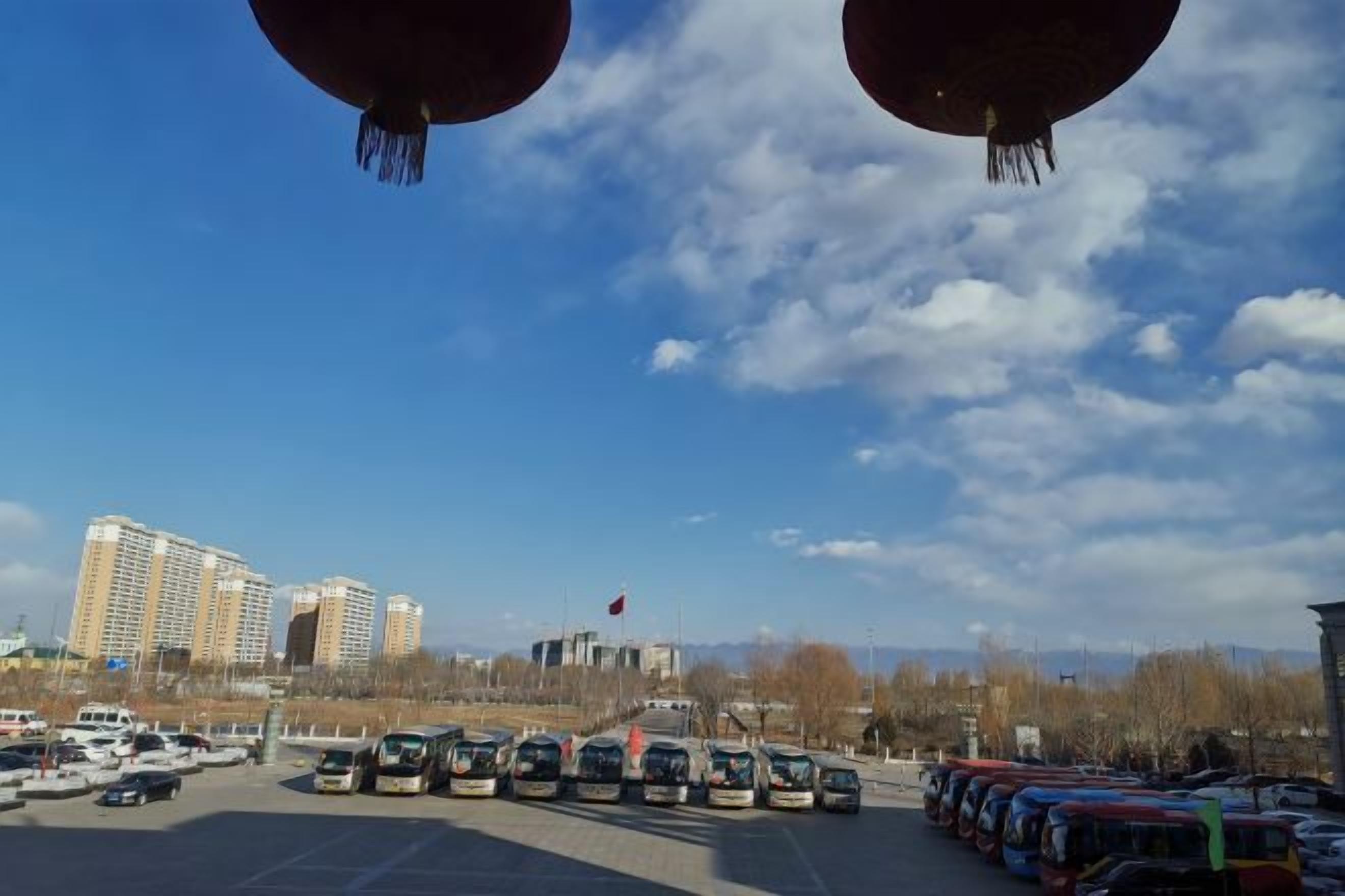 A parking lot with buses and cars, buildings in the background, and a clear sky.