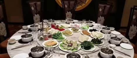 Una mesa redonda de comedor con diversos platos y tazones, rodeada de sillas.