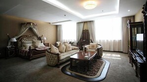 A well-lit room with a bed, sofa, and armchair, a television, and a chandelier.