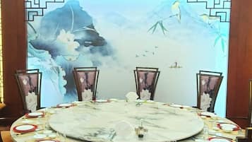 A round table set with a white marble top, surrounded by chairs with floral patterns, against a backdrop of a traditional Chinese painting.