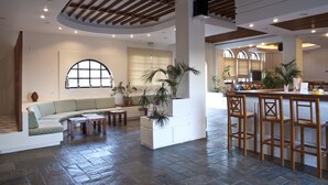 A spacious living area with a curved ceiling, a built-in bar with stools, a seating area with a sofa and coffee table, and a large window with a view. - Albatross Hotel (Platanias)