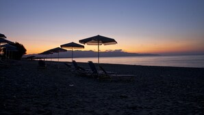 A beach with lounge chairs and umbrellas, a calm sea, and a sunset sky. - Albatross Hotel (Platanias)