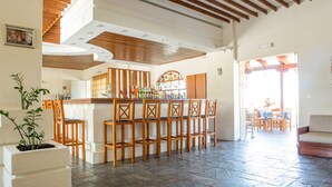 A spacious living area with a bar, wooden furniture, and a potted plant. - Albatross Hotel (Platanias)