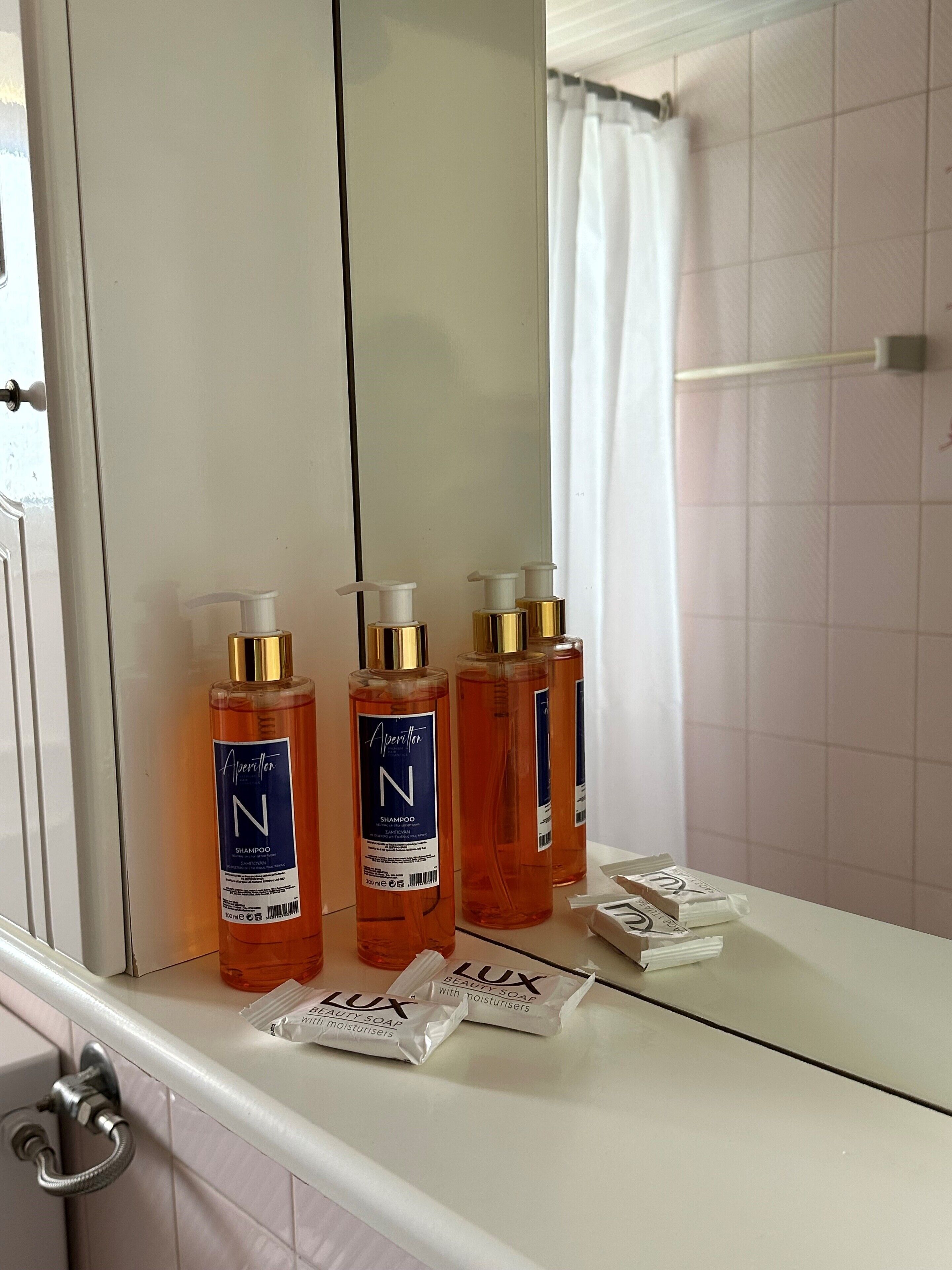Un baño con un lavamanos blanco, tres botellas de champú para el cabello y dos pastillas de jabón de belleza.