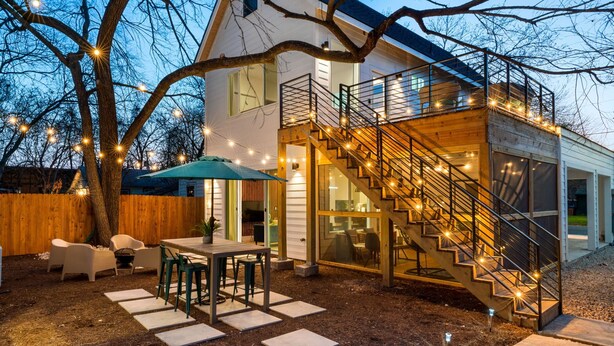 A modern house with a wooden deck, outdoor seating, and a staircase leading to a second floor. - Cozy Deck • Fire Pit • EV Charger • Outdoor Dining (Austin)