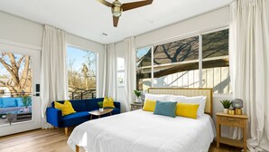 A bedroom with a large bed, a blue sofa, and a window with curtains. - Cozy Deck • Fire Pit • EV Charger • Outdoor Dining (Austin)