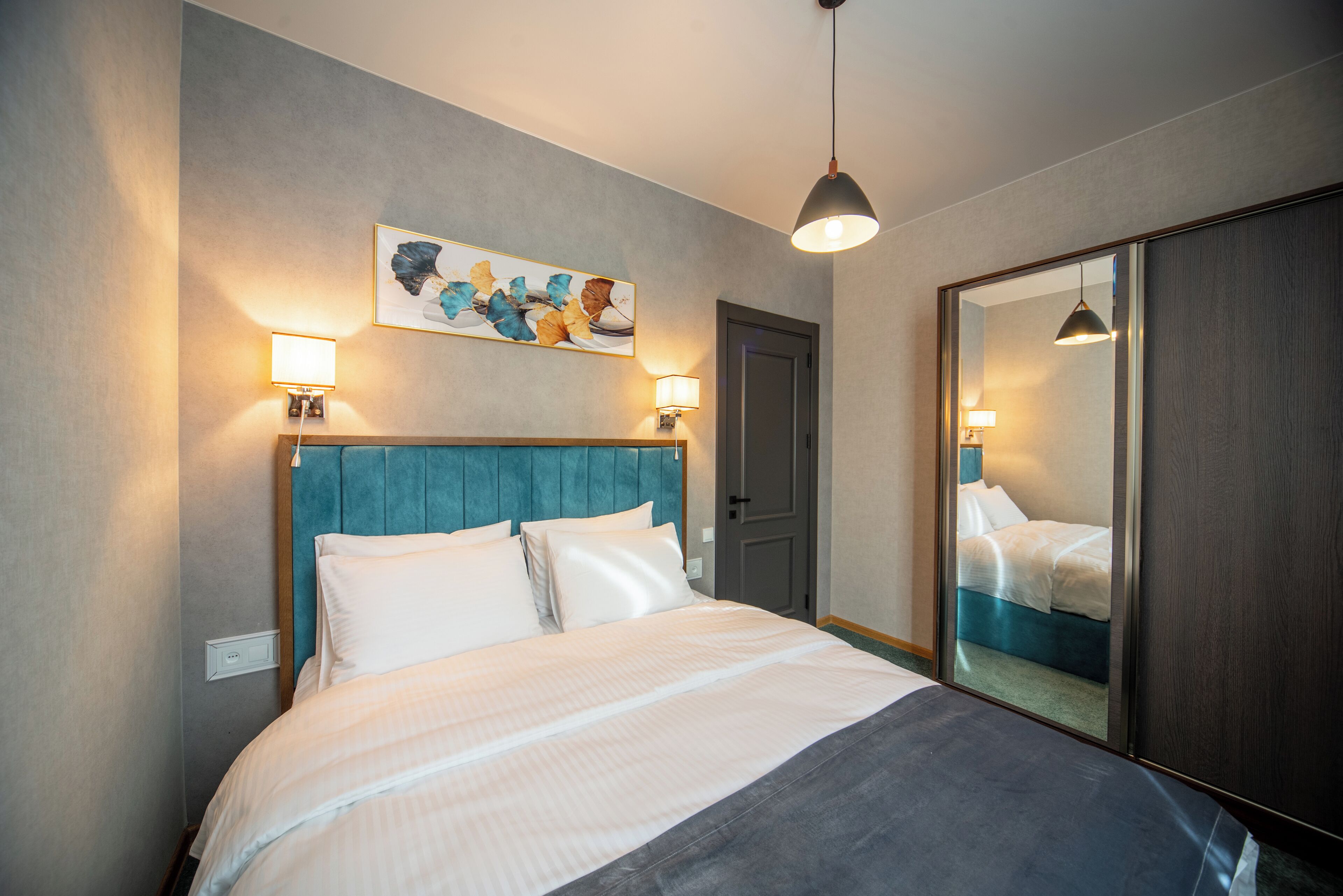 Una habitación de hotel con una cama, cabecera, una obra de arte colgada en la pared y un espejo.