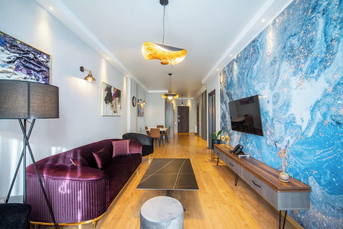 A modern living room with a purple sofa, a coffee table, and a TV on the wall.