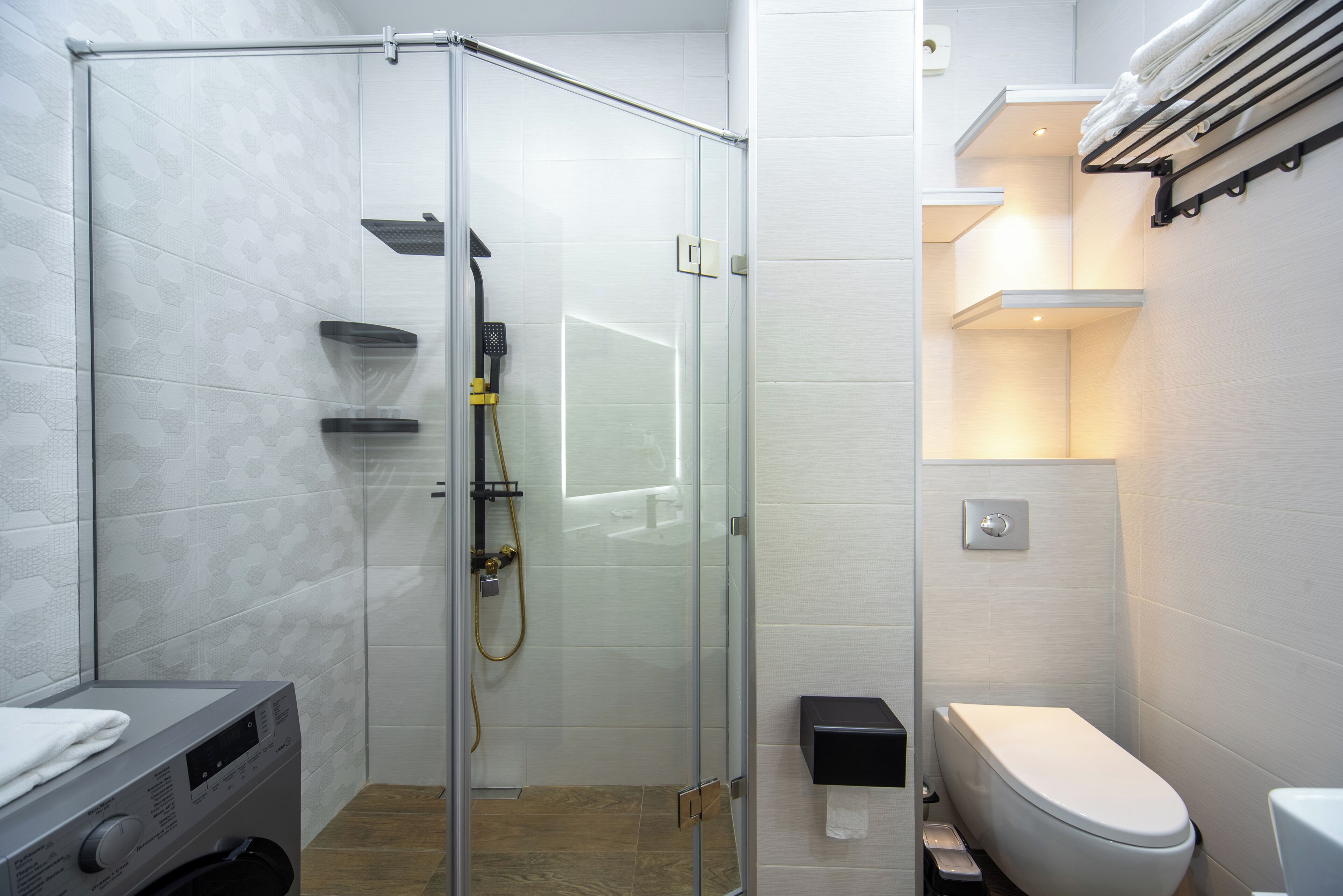 Un baño moderno con ducha envuelta en vidrio, inodoro y lavadora integrada.