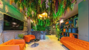 Un vestíbulo con sofás anaranjados, un mostrador de recepción y una pared verde con plantas colgantes.