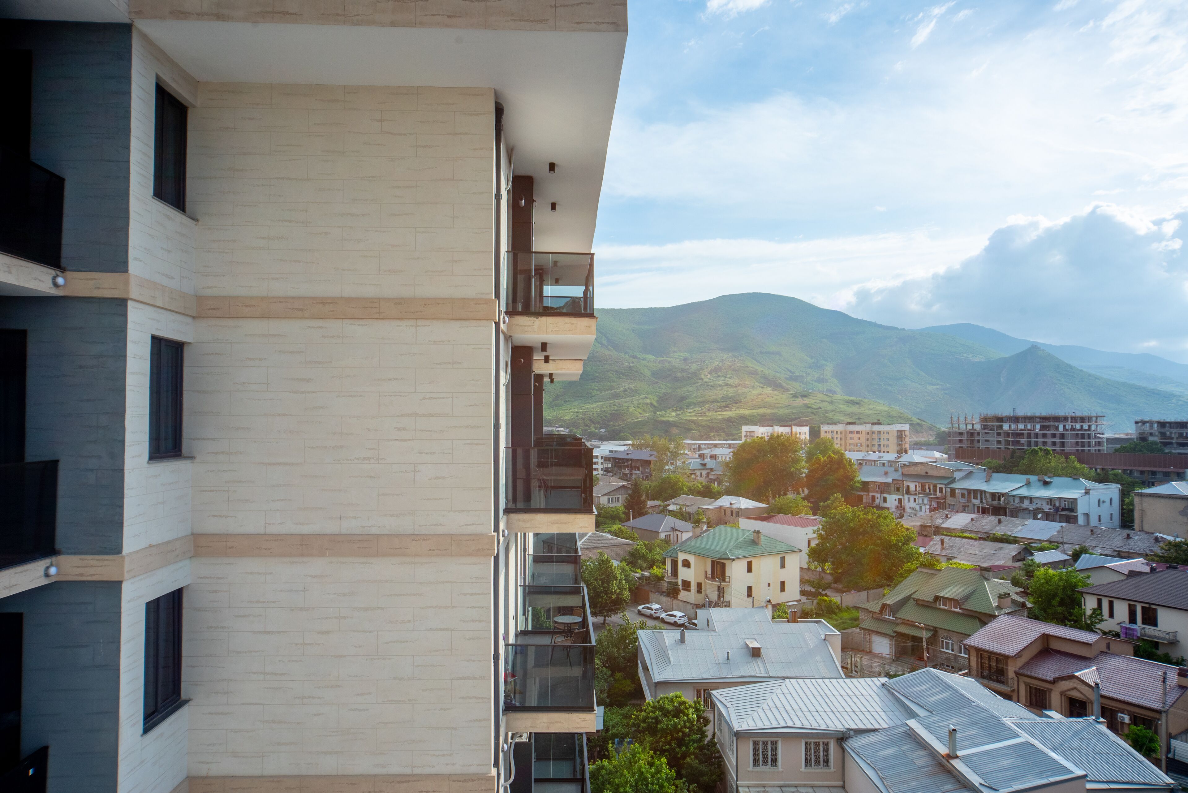 A modern building with multiple balconies overlooking a town with mountains in the background.