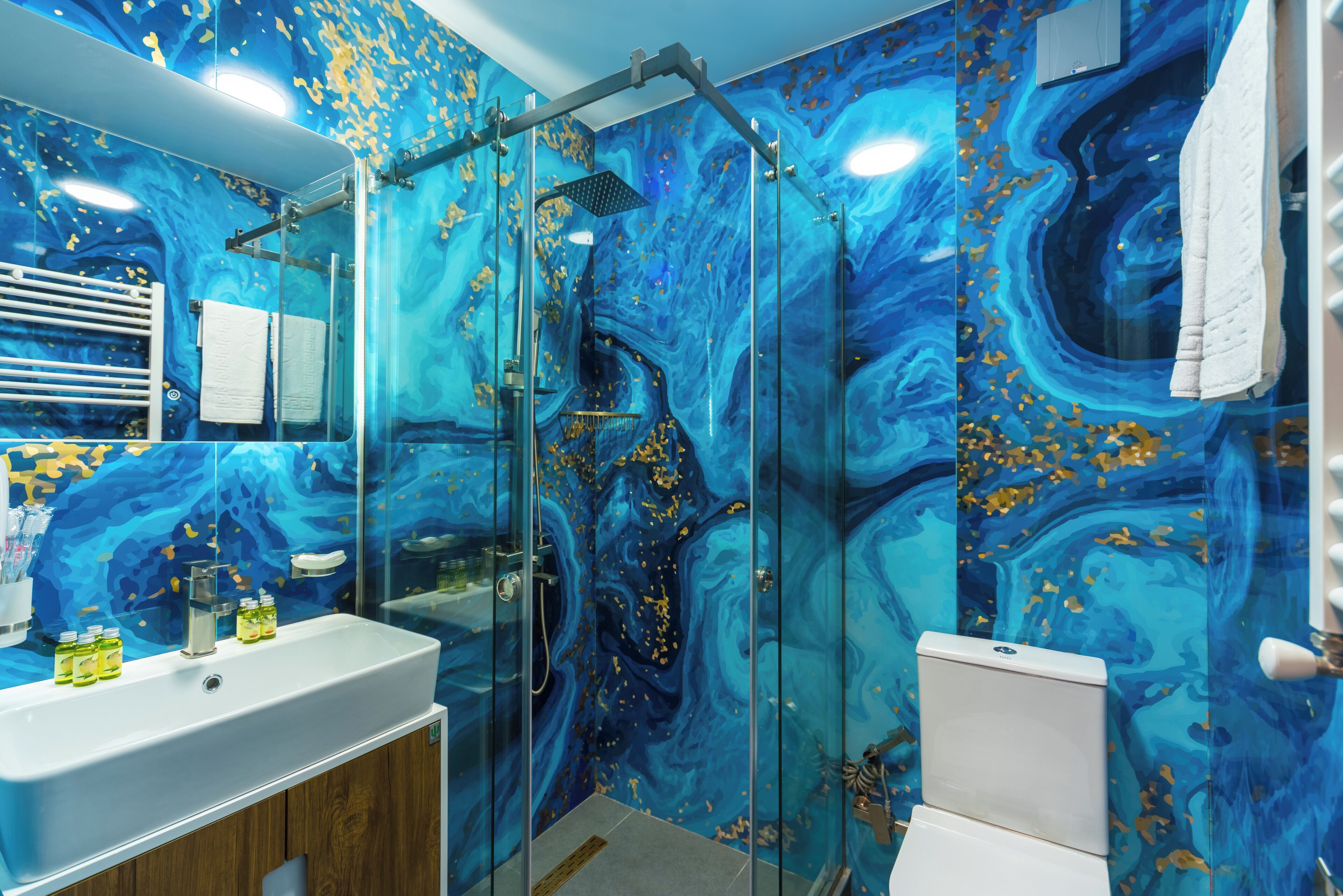 Un baño con ducha envuelta en vidrio, lavamanos blanco y pared con diseño de mármol.