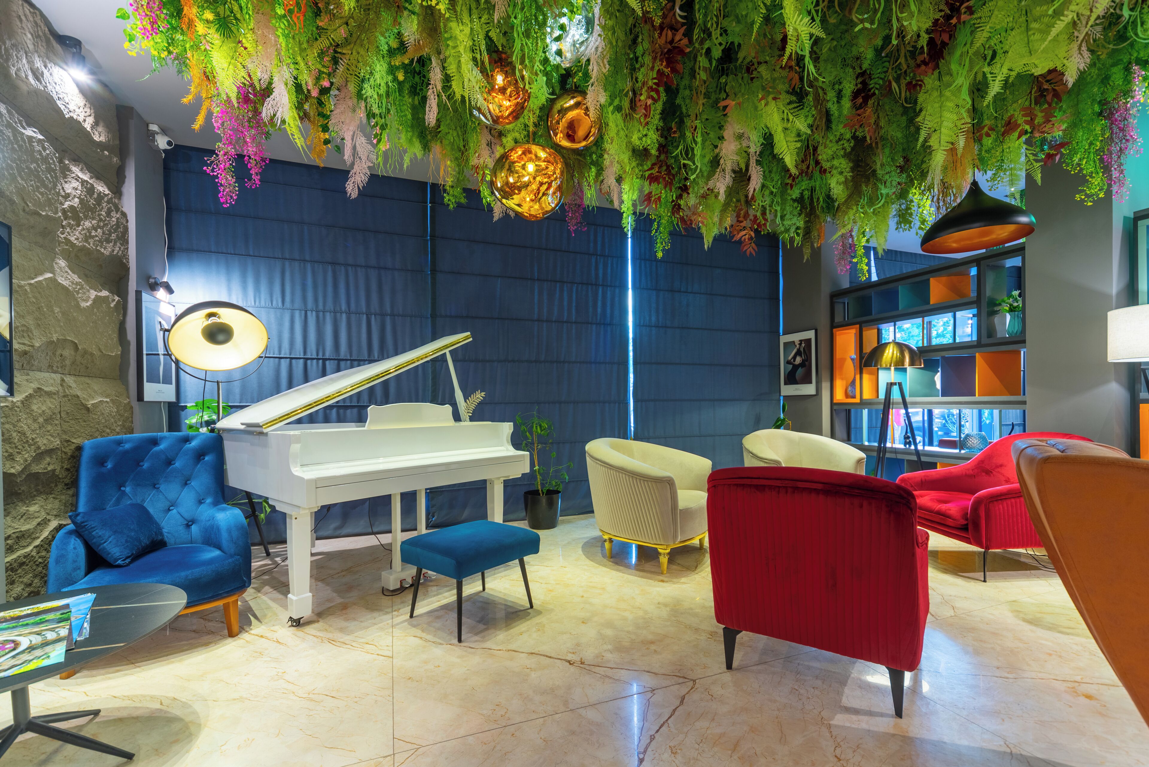 A room with a grand piano, plush seating, and a ceiling adorned with hanging plants and decorative lights.