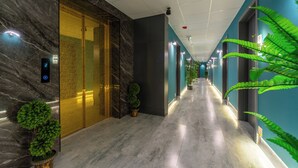 Un pasillo moderno de hotel con paredes de mármol, un panel de control de ascensor digital y plantas en macetas.