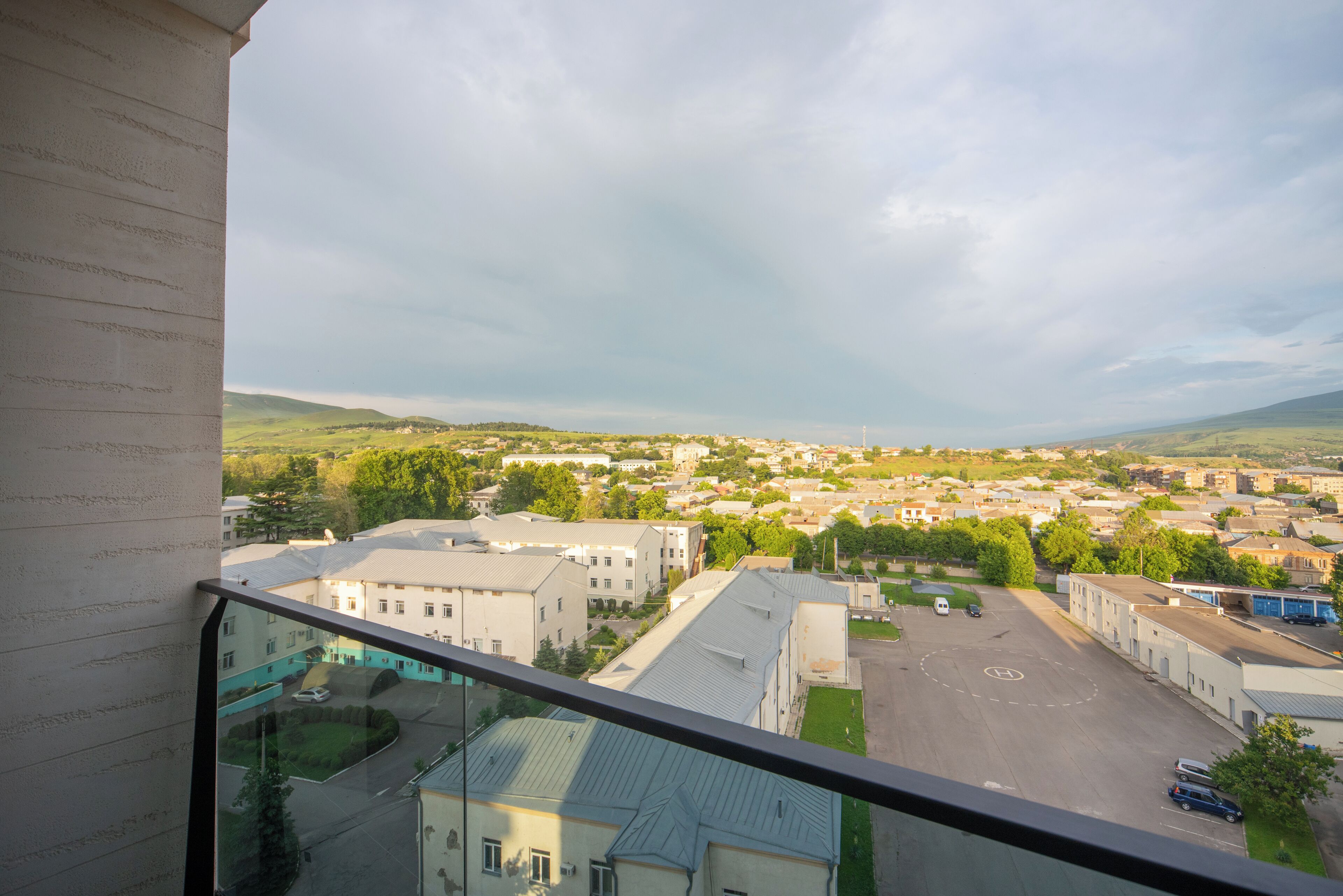 A view from a balcony overlooking a town with buildings, a parking lot, and green hills in the distance.
