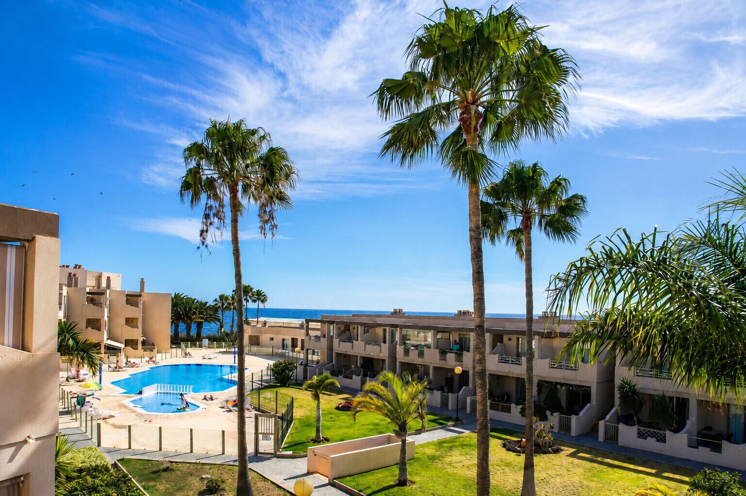 A hotel with a swimming pool, palm trees, and a view of the sea.