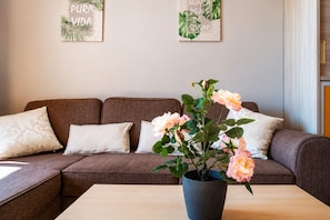 Un salon avec un canapé marron, deux coussins blancs, une table basse en bois et une plante en pot ornée de fleurs roses.