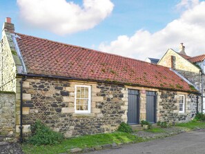 A stone building with a red-tiled roof, a small window, and a door.