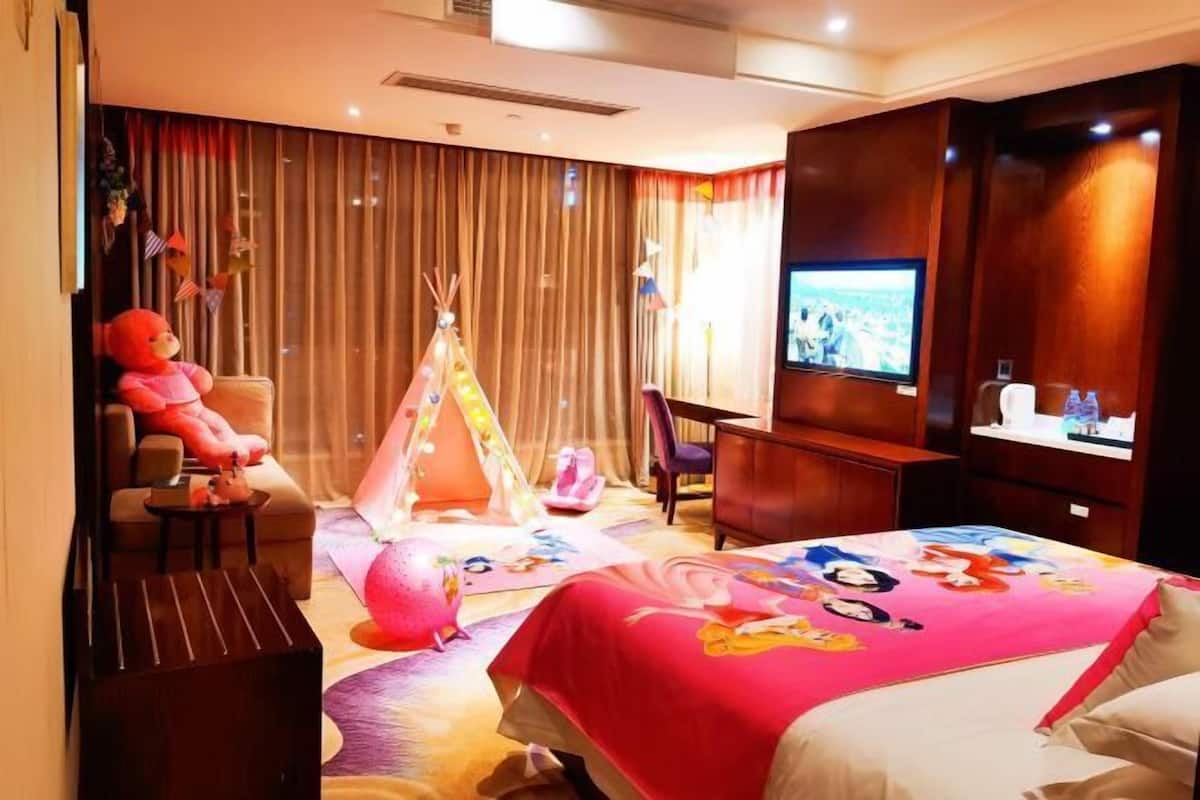 A hotel room with a bed, a TV, a teddy bear, a tent, and a chair.