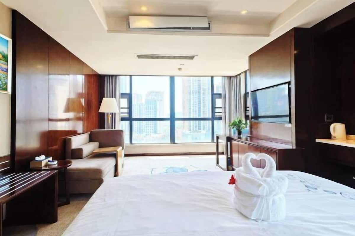 A hotel room with a bed, a TV, a desk, a chair, and a view of the city.